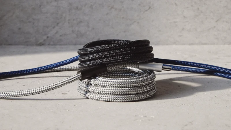 Tre flettede USB-C-kabler i forskellige farver, rullet løst på beton