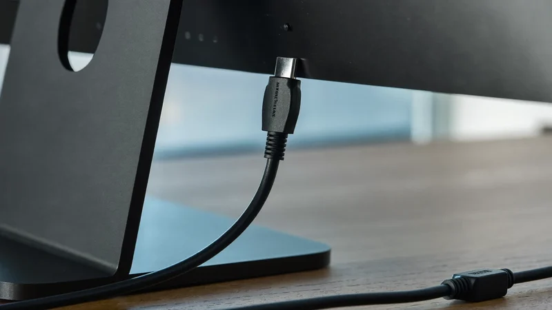 Sort HDMI-kabel tilsluttet bagsiden af en skærm på et rent skrivebord